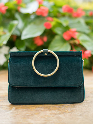 a dark emerald green velvet purse with a gold bracelet handle perfect for holiday party outfits and winter wear
