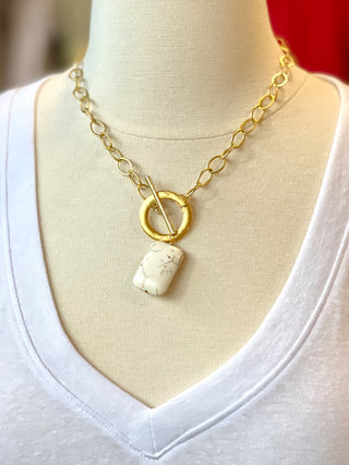 a large gold chain link necklace with a white rectangular stone pendant and gold circle front clasp