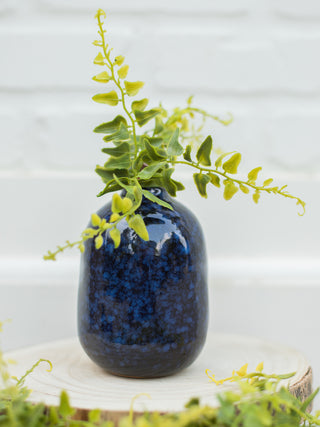 a dark blue vase with black streaks shown with faux foliage