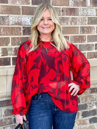 a sheer red blouse in floral print with long statement sleeves and ruffle details perfect for holiday season fashion