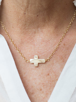 a gold cable chain necklace with a mother of pearl cross on its side