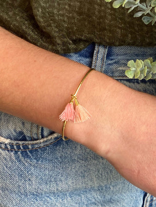 a gold cuff bracelet with double tassels in pink and peach worn on a wrist