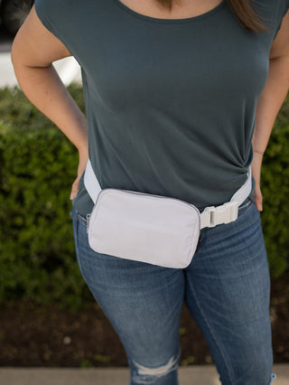 a white sling bag with zip closure and three pockets for your necessities worn as belt bag fanny pack