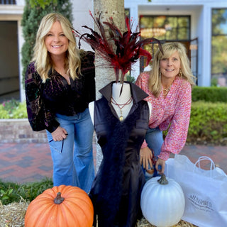 two women smiling from behind pumpkins and scarecrow for charity