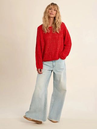 Woman wearing a red sweater with sparkles and light blue jeans