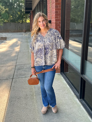 a chinoiserie print blouse in blue with ruffle details and puff sleeves in a feminine and lightweight cut shown with denim