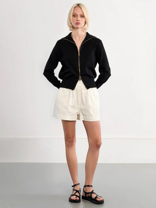 Person wearing a black zip-up jacket and white shorts on a plain background