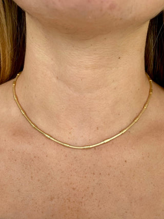 a gold necklace made with tubular beads that drapes above the collarbone