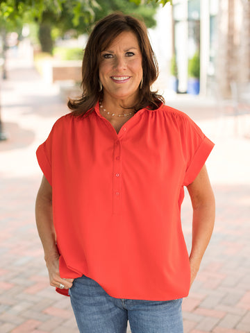 a red orange half button up blouse with short sleeves and a tie at the hem