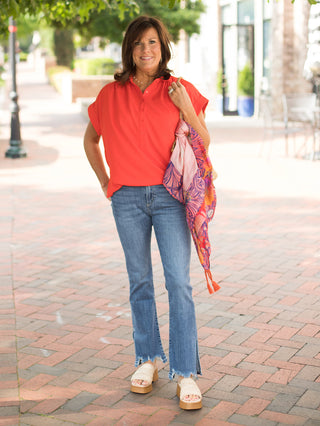 a red orange half button up blouse with short sleeves and a tie at the hem shown with denim pants