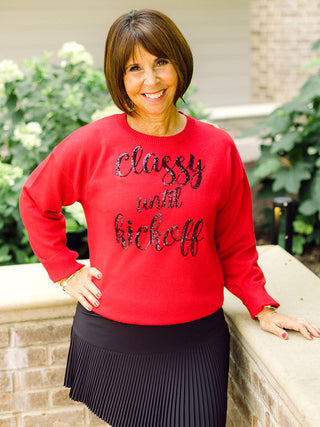 a red sweater with black sequin lettering that reads classy until kickoff perfect for football games and tailgating