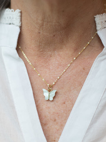 a stackable necklace featuring a sea foam aqua green butterfly charm along a gold chain with white enamel beads