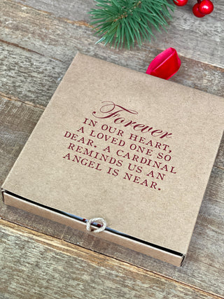 a gift box with a red and white cardinal disc ornament that says forever in our hearts