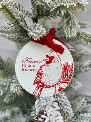 a gift box with a red and white cardinal disc ornament that says forever in our hearts