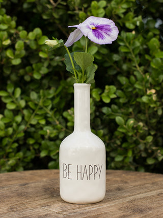 a mottled ceramic white bud vase with creamy glaze and debossed sentiment that reads be happy