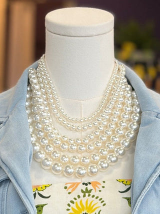 Mannequin wearing a light blue denim jacket, floral dress, and multiple pearl necklaces.