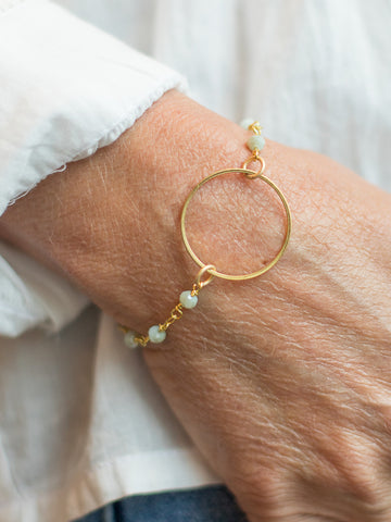 a bracelet with sea foam color crystal beads along a gold cable chain with a circle charm at the center