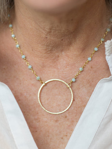 a statement necklace featuring sea foam aqua green crystal beads along a gold chain with a 24k gold plated circle charm