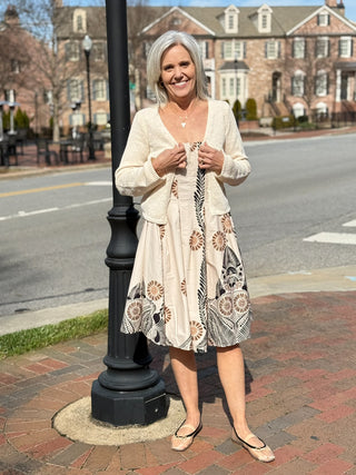 a soft ivory cream cropped knit cardigan with front hooks worn over a cream patterned dress