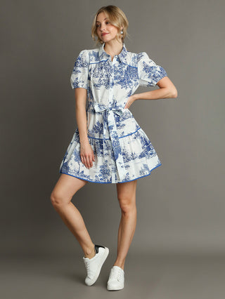 elegant blue toile mini dress with charming landscape print and self tie belt worn with white sneakers