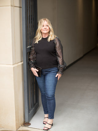 a black sweater with sheer metallic statement sleeves perfect for fall and winter fashion shown with denim pants