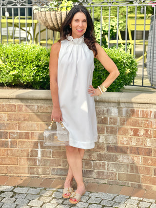 classy high neck white mini dress with ruffled details and a sweet back bow tie worn with beige sandals