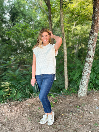 an off white cable knit sweater vest with short sleeves made to wear alone or layer in the fall and winter shown with denim