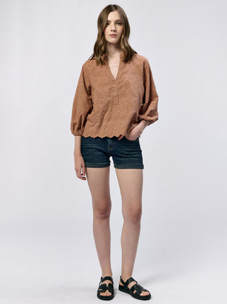 brown eyelet blouse with v neckline poet sleeves and cinched back paired with dark wash denim shorts