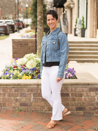 fashionable cropped denim jacket with frayed hem and metallic buttons worn with white pants