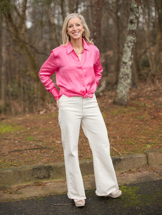 hot pink button down silk blouse with long sleeves and tie waist shown with cream wide leg denim
