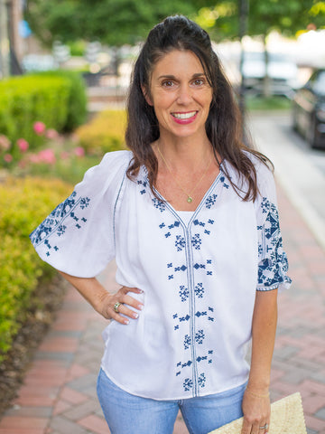 a white blouse with blue embroidery featuring three quarter length sleeves and a v neckline
