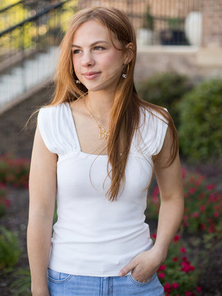 a stretch knit white top with a square neckline and ruched shoulder detail along the cap sleeves