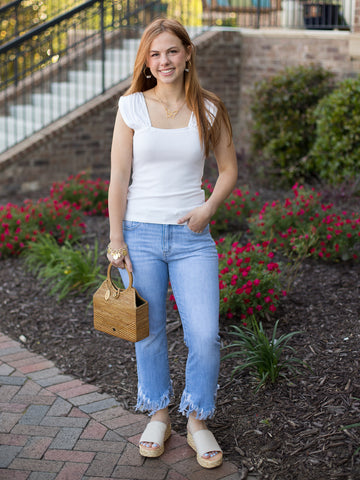 a stretch knit white top with a square neckline and ruched shoulder detail along the cap sleeves shown with denim pants