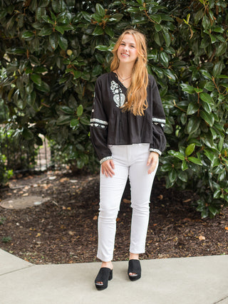 a boho chic blouse with white embroidery on the black long sleeve top perfect for fall fashion shown with white pants