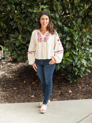 a boho chic blouse with red embroidery on the cream long sleeve top perfect for fall fashion shown with denim pants