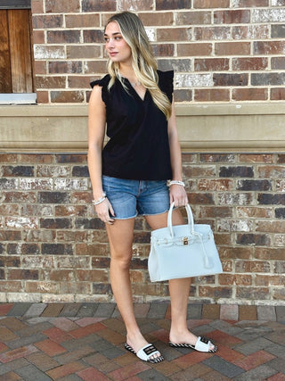 tan sleeveless blouse with ruffle details and v neckline paired with blue denim shorts
