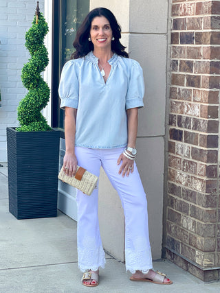 light blue shirred puff sleeve top with ruffled v neck worn with white pants