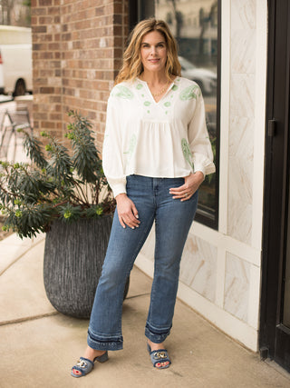 long sleeve loose fit cream v neck blouse with green embroidery design worn with dark blue jeans