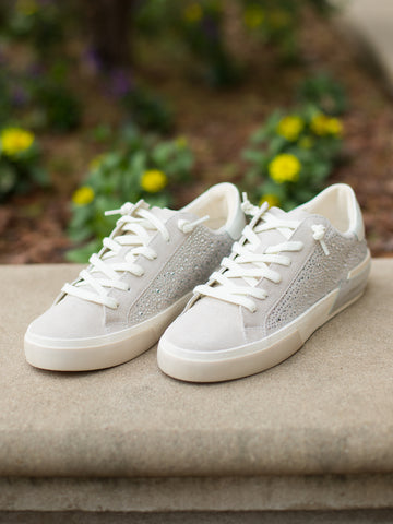 a pair of suede sneakers in a low top style in ivory with crystal studding along the sides