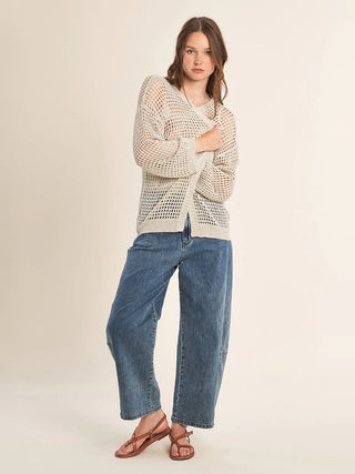 Woman wearing a beige textured sweater and blue jeans on a white background