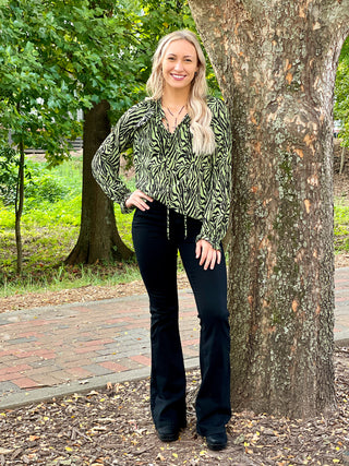 a loose fitting animal print top in green and black with feminine long sleeves and pleated fabric shown with black pants