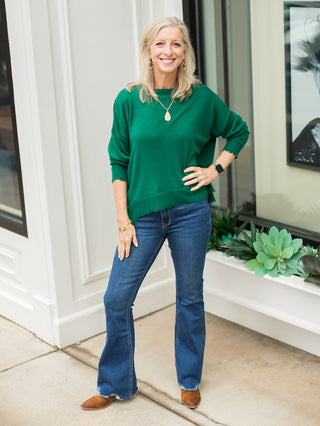 a classic green crewneck sweater with raw edges and relaxed fit long sleeves perfect for errands shown with denim