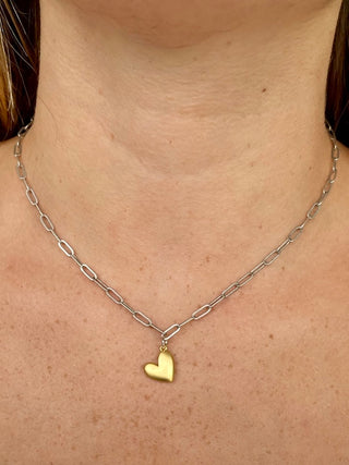 a mixed metal necklace featuring a gold heart charm on a silver chain 