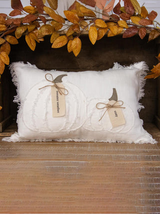 white pillow with decorative tags on a wooden surface with autumn leaves in the background