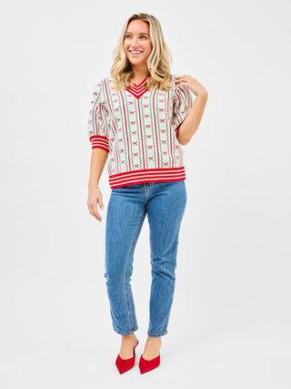 a cute white holiday sweater top with red and green stripes and bow ties worn with blue jeans