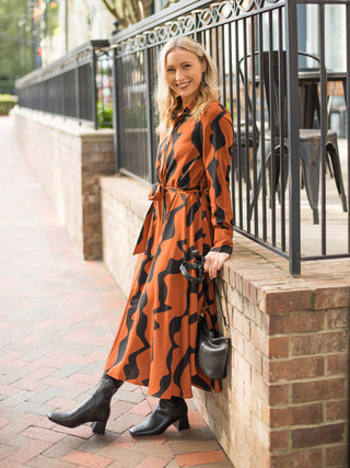 a retro printed midi dress in orange and black with long sleeves perfect for modest dressing shown with black boots