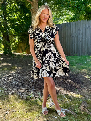 a black and cream twirly mini dress with a v neck and ruffled short sleeves worn with gold sandals