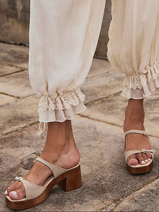 Beige sandals worn with white pants on a stone pavement.