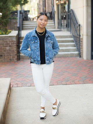 a jean jacket that crops at the waist perfect for layering in fall winter spring and summer shown with white pants