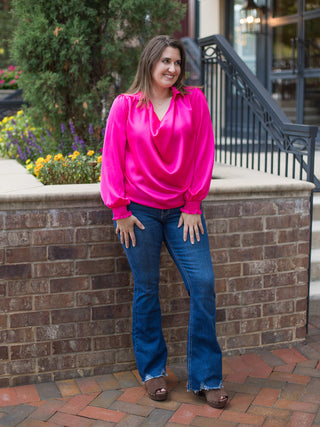 a long sleeve satin blouse in hot pink with draped details perfect for summer to fall fashion shown with denim pants